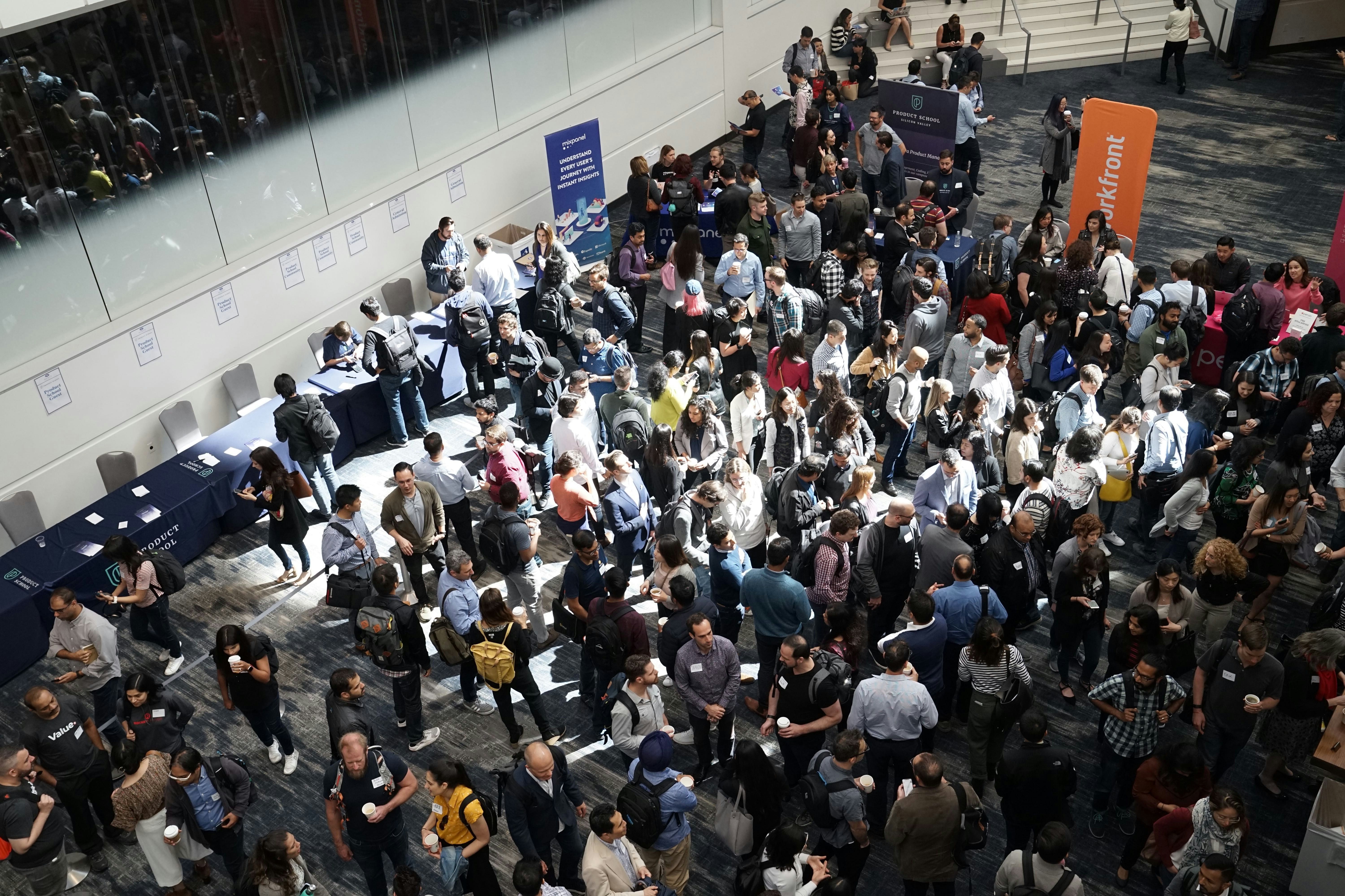 A crowded tech conference expo hall, attendees networking between sponsor booths